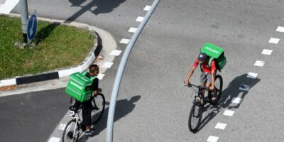 Grab delivery cyclists ride past each other in Singapore on April 20, 2020. (Photo by ROSLAN RAHMAN / AFP)